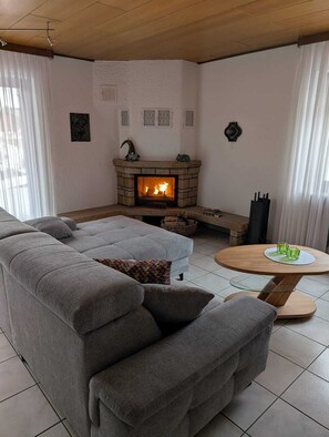 Uma sala de estar moderna com lareira de pedra, sofá modular cinza e mesa de centro redonda de madeira.