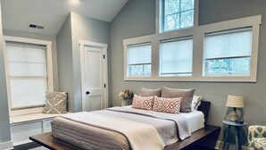 Une chambre avec un grand lit, un coin fenêtre aménagé en siège, une table de chevet et une lampe.