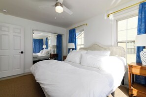 Ein Hotelzimmer mit zwei Betten, einem Deckenventilator, einem großen Fenster mit blauen Vorhängen und Blick nach draußen.