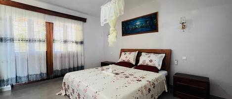 Una camera da letto con un letto grande, due comodini, un tavolino, una finestra con tende e una lampada a parete.