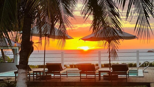 A poolside area with lounge chairs and umbrellas, overlooking a sunset over the ocean. - Nosy Bay View (Nosy Be)