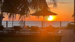 A sunset view from a beachside lounge with lounge chairs and a palm tree. - Nosy Bay View (Nosy Be)