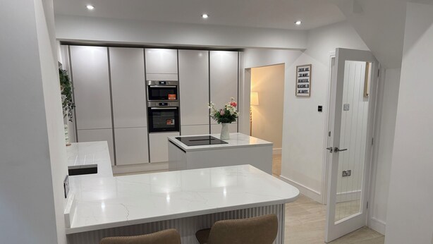 A modern kitchen with white cabinetry, a central island with stools, built-in ovens, and a refrigerator.