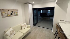 A modern living room with a white sofa, a dining table with chairs, and a kitchen area visible through an open door.