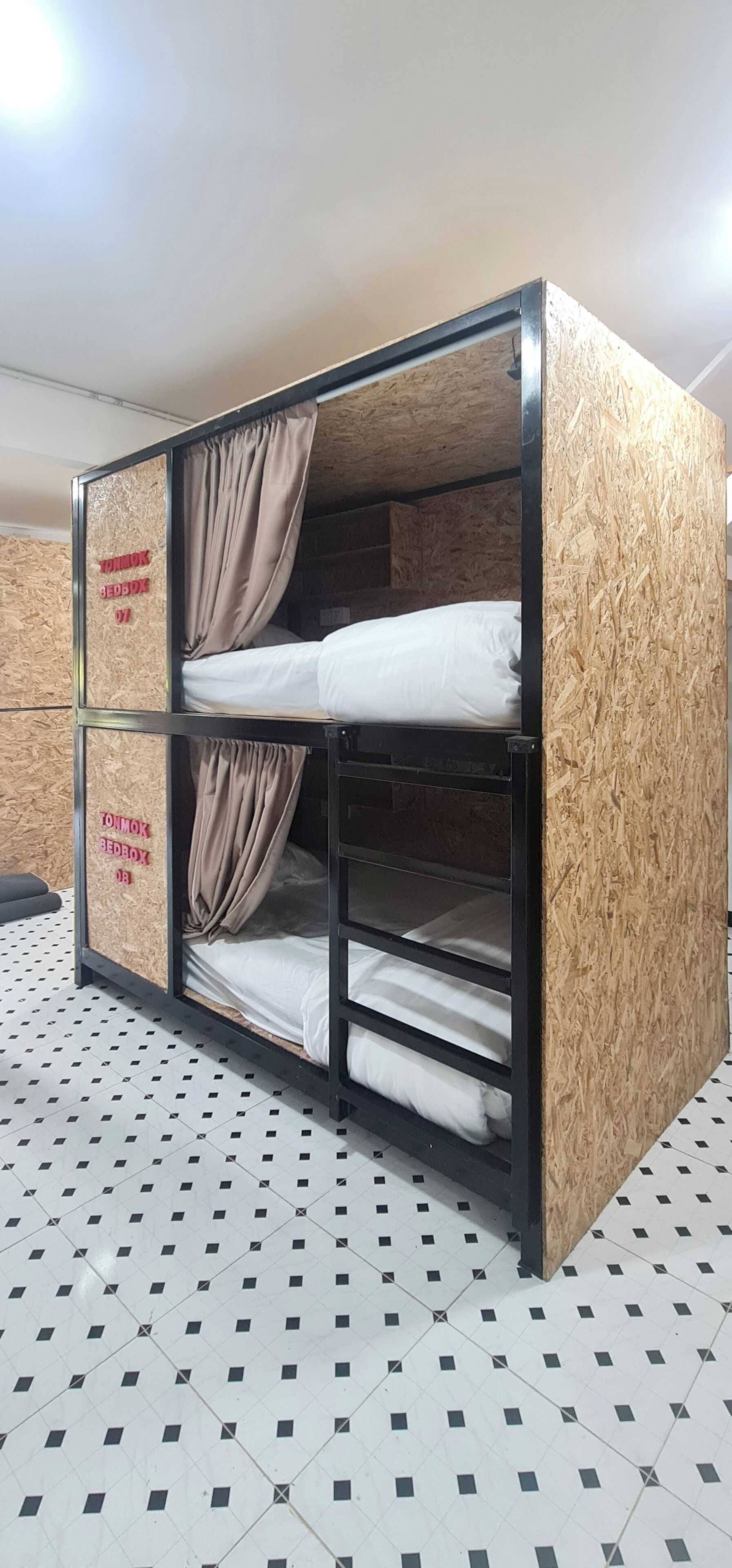 A bunk bed with two levels, each with a mattress and a curtain. The bed is made of wood with a textured surface.