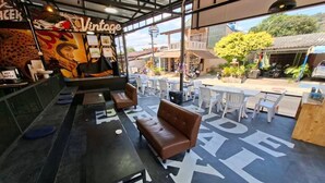 Een terras met tafels en stoelen, een bar met een antiek bord, en een ruim buitengebied met uitzicht op de straat.
