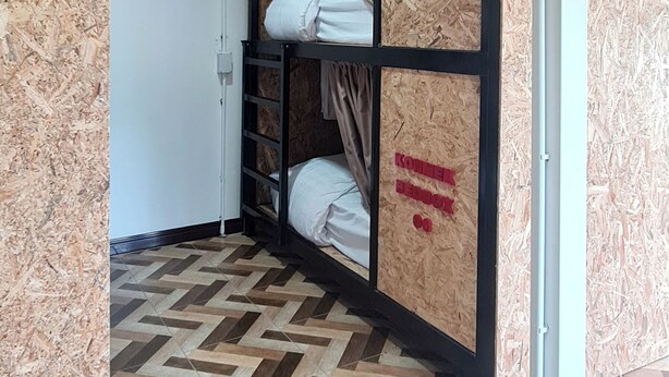 Een kamer met een visgraatvloer, een stapelbed met hoofdeinde, en een muur met een 'KONINKEL BEDBOX' bordje.