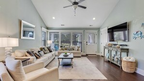 A spacious living room with a sectional sofa, a coffee table, and a ceiling fan. - Salt Air Cottage - Private Pool, Dog Friendly, 4 Blocks to Beach (Carolina Beach)