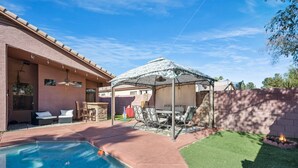 Ein Garten mit Schwimmbecken, Terrassenmöbeln, einer überdachten Sitzgruppe und einer Feuerstelle.