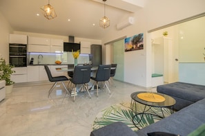 A modern kitchen with white cabinets, a dining area with a glass table and chairs, and a living area with a sofa and a coffee table. - Tranquil Country Villa in Naklice for 6 (Omis)