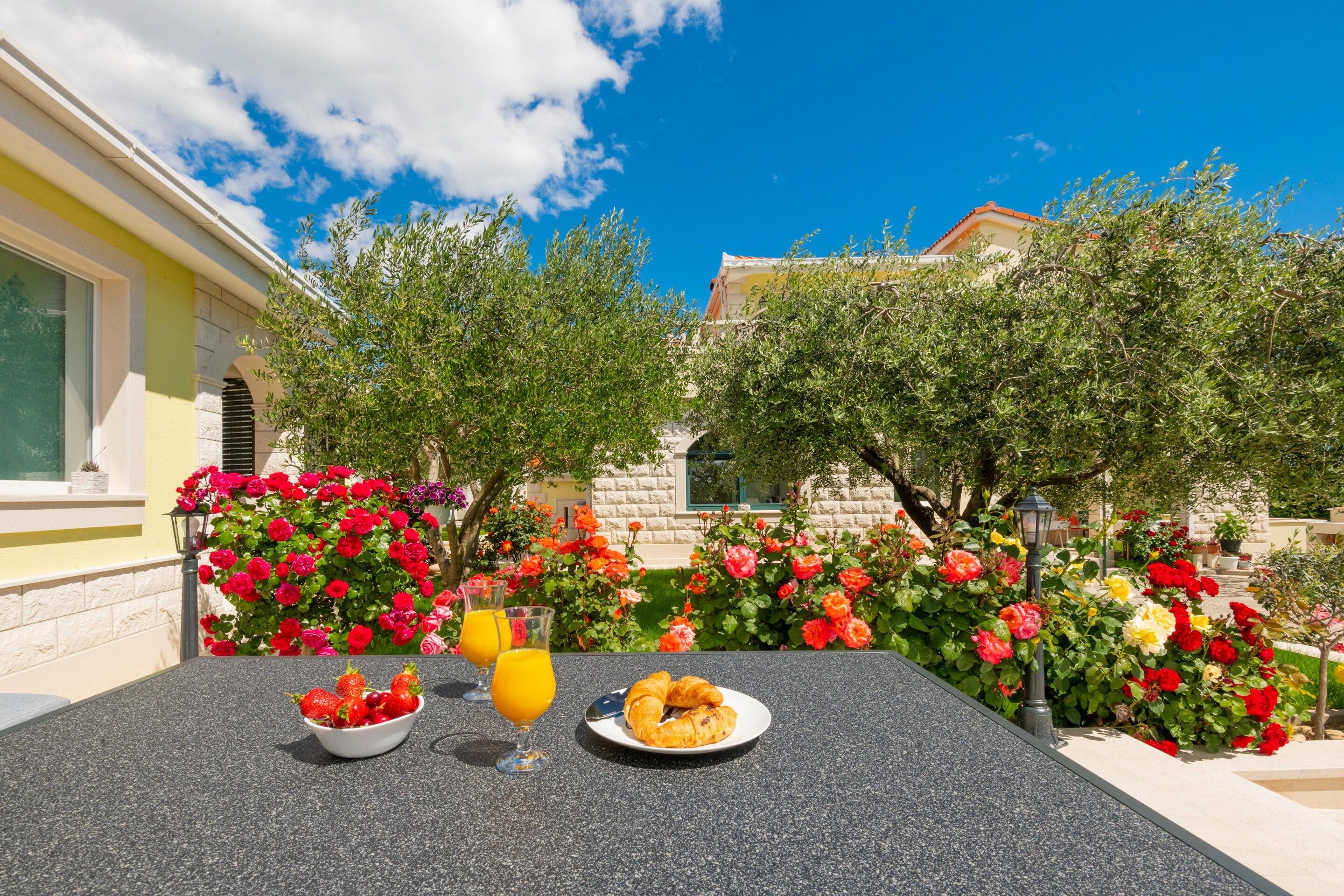 An outdoor dining area with a table set for breakfast, including strawberries, orange juice, and croissants.