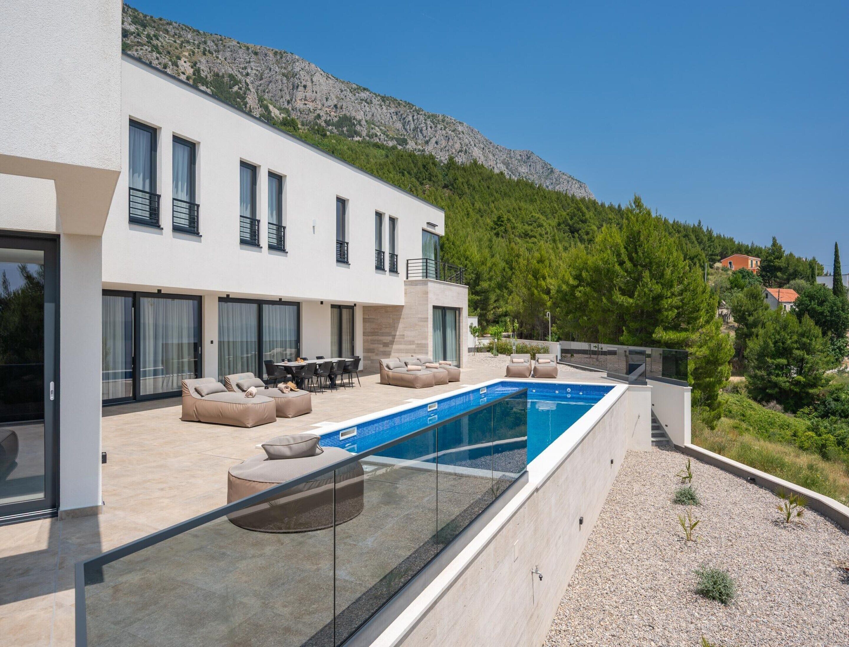 Eine moderne Villa mit Schwimmbad, Sitzgelegenheiten im Freien und Blick auf die Berge.
