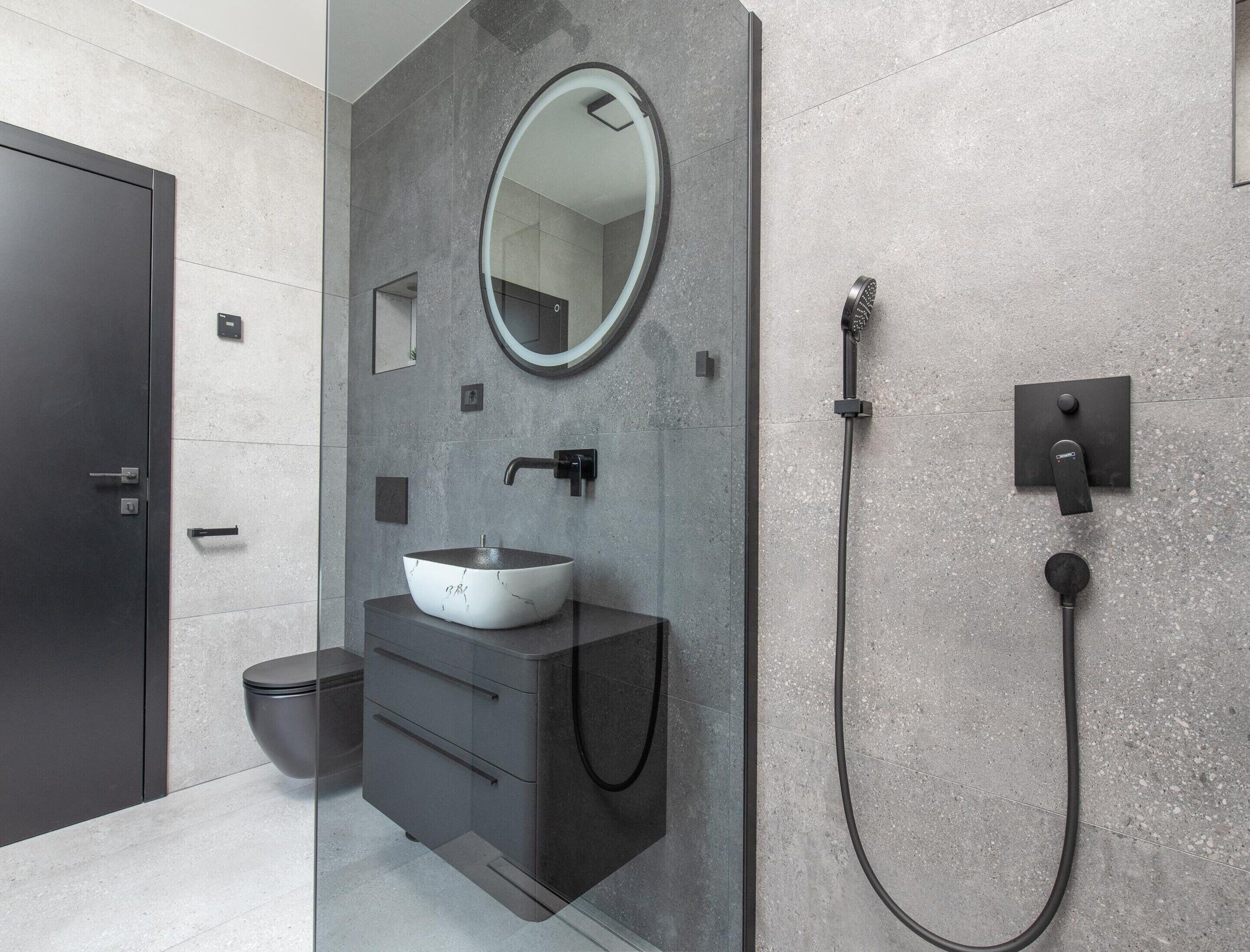 Une salle de bain moderne avec un miroir rond, un lavabo sur colonne, une douchette à main et des toilettes.