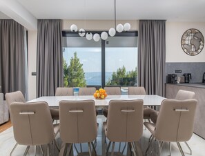 A modern dining room with a glass table, six chairs, a fruit bowl, and a view of the sea. - Luxury Seaview Villa With Jacuzzi for 10 (Imotski)