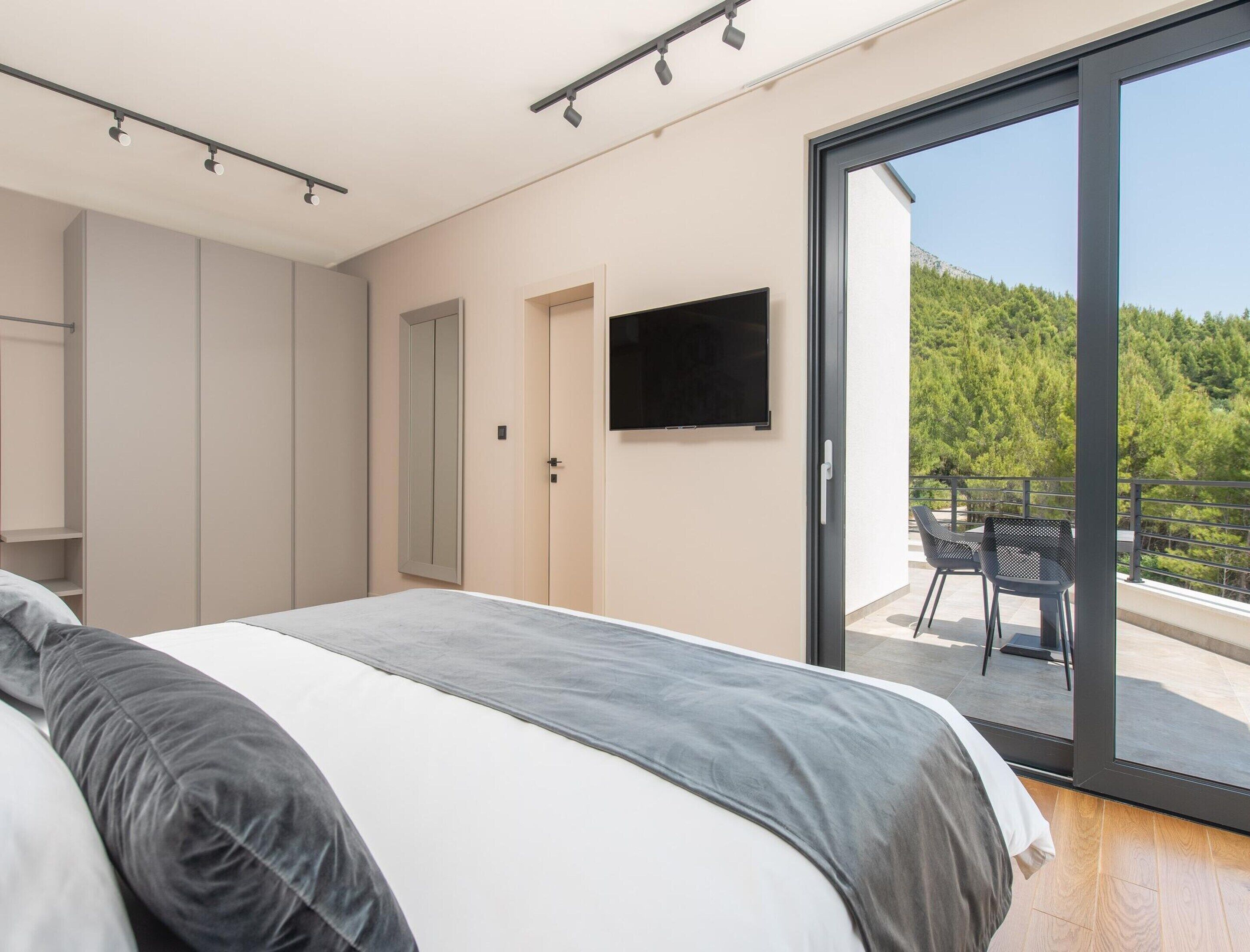 A bedroom with a bed, a TV, a sliding glass door to a balcony, and a wardrobe.