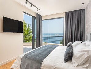 A modern bedroom with a large bed, a TV mounted on the wall, and a balcony with a view of the sea. - Luxury Seaview Villa With Jacuzzi for 10 (Imotski)