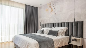 Ein modernes Schlafzimmer mit einem großen Bett, einem Kopfteil, Nachttischen und einer Wand mit strukturierter Wandgestaltung.