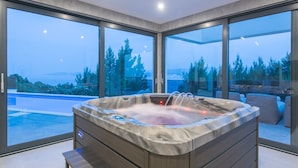 Ein modernes Badezimmer mit einer freistehenden Badewanne, großen Fenstern und Blick auf Pool und Bäume.