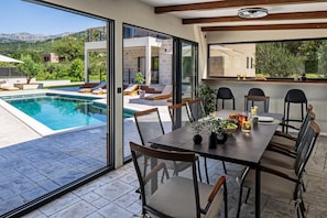 A dining area with a view of a swimming pool and mountains. - Stylish 4-Bedroom Villa Agrosa with 30 m2 Private Pool, Hydromassage, Finnish Sauna and Fun zone (Srinjine)