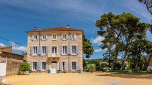 A two-story building with a symmetrical facade, a central entrance with a balcony, and a surrounding gravel area. - Villa Roubia Hôtel & Spa (Roubia)