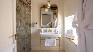 A bathroom with a marble wall, a white sink with gold fixtures, a mirror with a gold frame, and a chandelier. - Villa Roubia Hôtel & Spa (Roubia)
