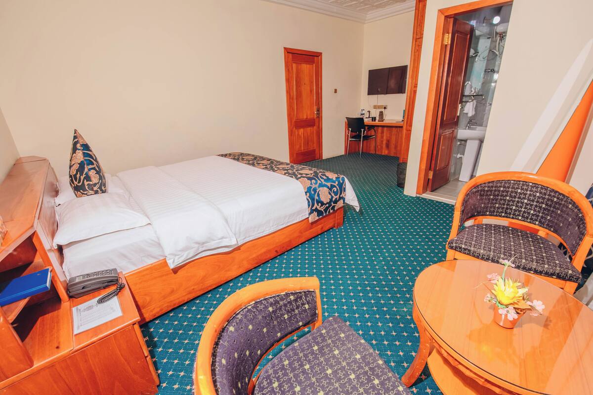 Ein Hotelzimmer mit einem Bett, einem Schreibtisch, einem Stuhl und einem kleinen Tisch mit Blumenvase.