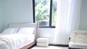Quarto com cama, cadeira e janela com cortinas.