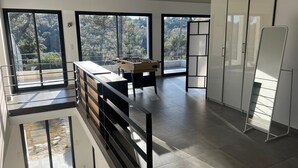 A spacious room with a foosball table, large windows, and a view of trees. - Modern architect-designed villa with pool - Immersion in nature & light (Roquefort-les-Pins)
