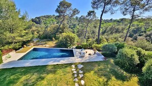 A swimming pool with a stone border, surrounded by lush greenery and trees. - Modern architect-designed villa with pool - Immersion in nature & light (Roquefort-les-Pins)