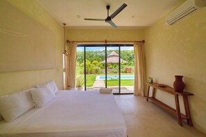 A bedroom with a bed, a ceiling fan, a window with curtains, a view of a pool and garden, and a small table with a vase. - Po Popoyo Private Pool Boutique Villa - Villa Sham (Popoyo)