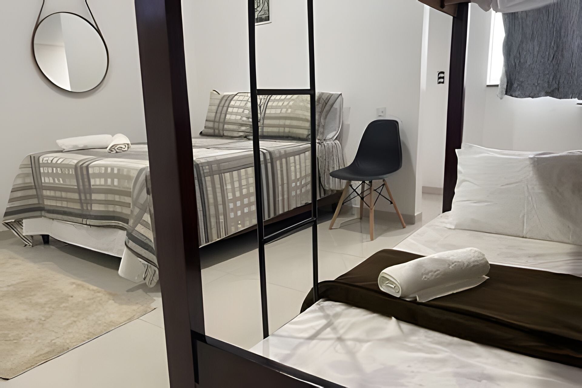 Un dormitorio con dos camas, una silla, un espejo y una ventana.