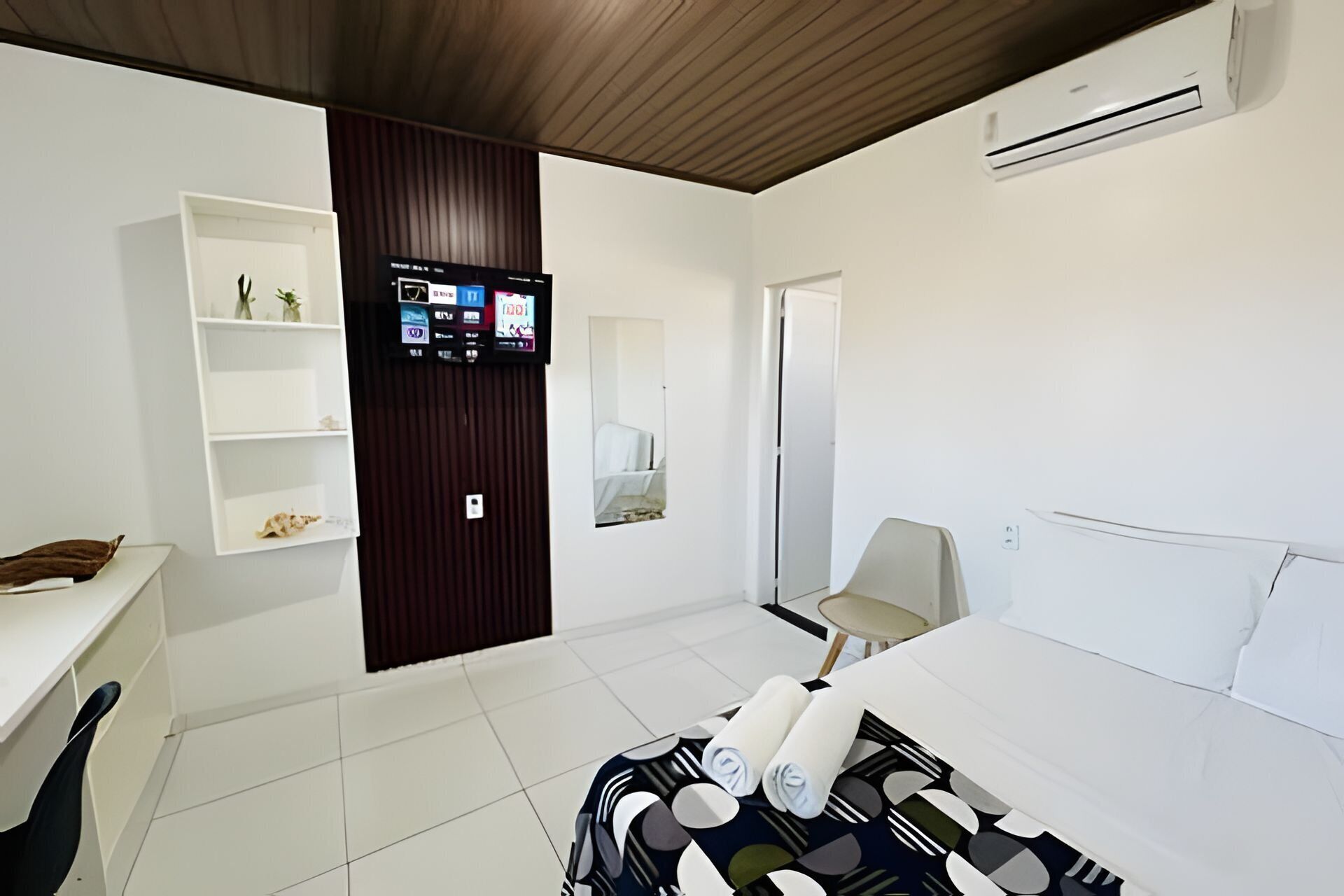 Een moderne hotelkamer met een bed, een aan de muur bevestigde televisie, een bureau en een stoel.
