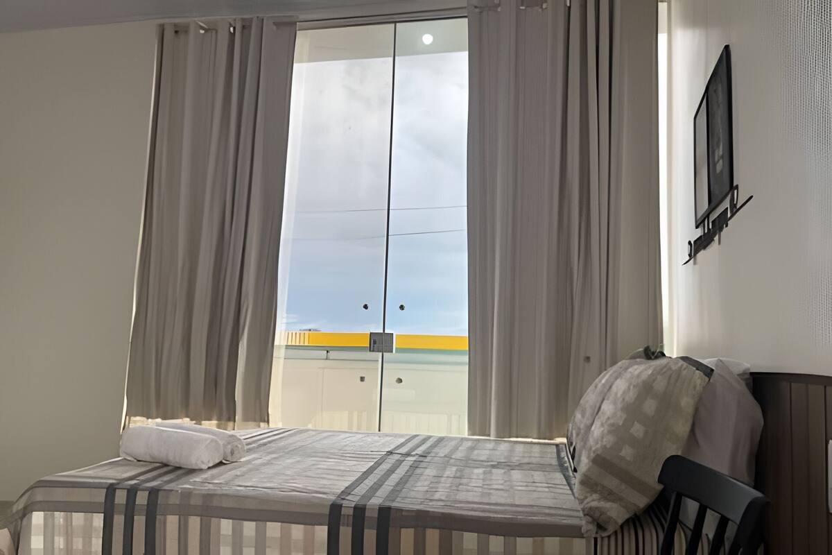Une chambre d’hôtel avec un lit, une fenêtre avec des rideaux, une vue sur un immeuble et un téléviseur fixé au mur.