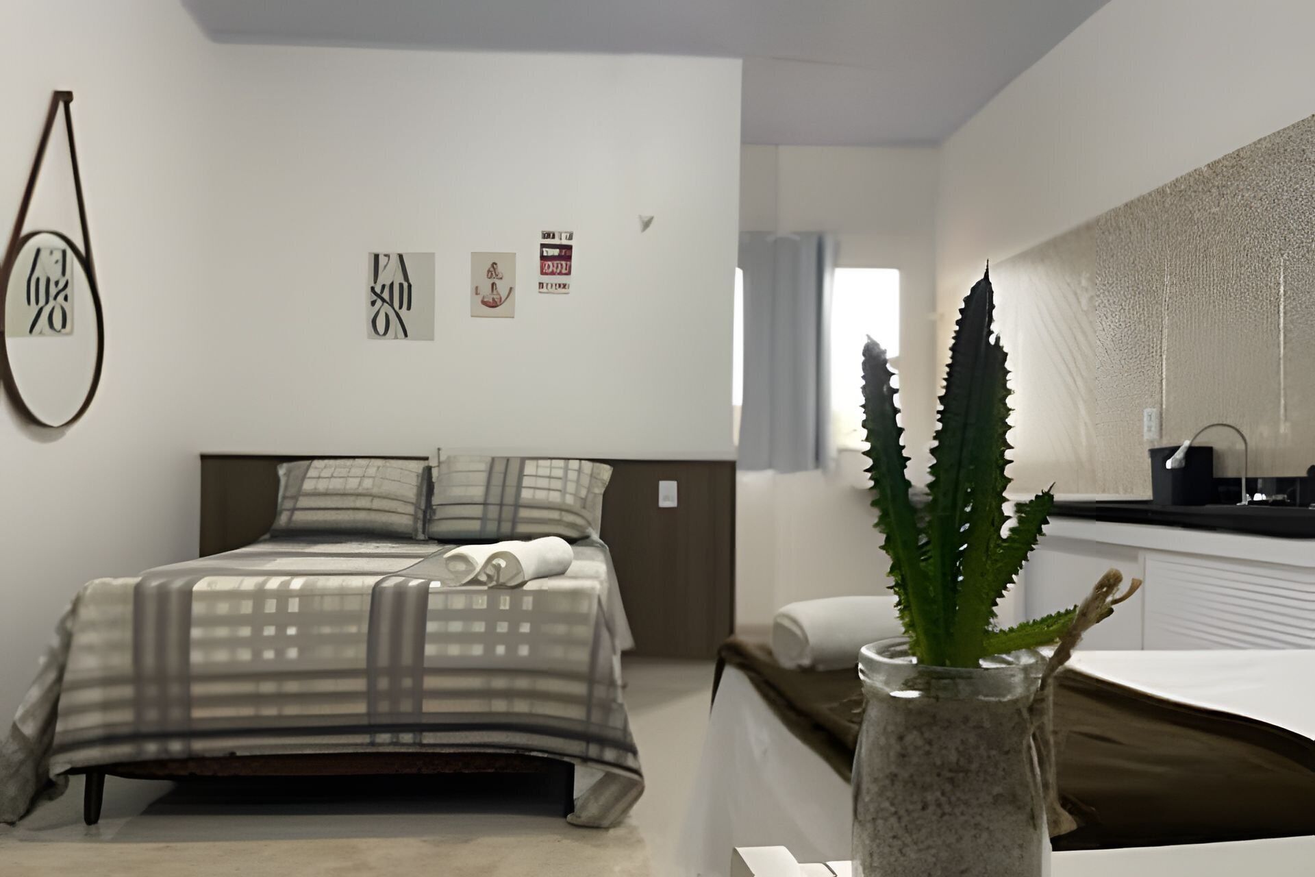 A bedroom with a bed, a bedside table with a vase, and a bathroom with a sink and mirror.