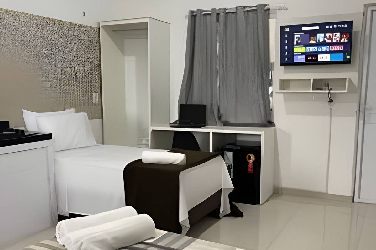 Une chambre d’hôtel moderne équipée d’un lit, d’un bureau avec un ordinateur, d’une télévision et d’un petit coin salon.