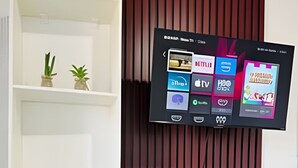 A wall-mounted TV displaying various channels and a shelf with decorative items. - Apartamentos Vitória (Barreirinhas)