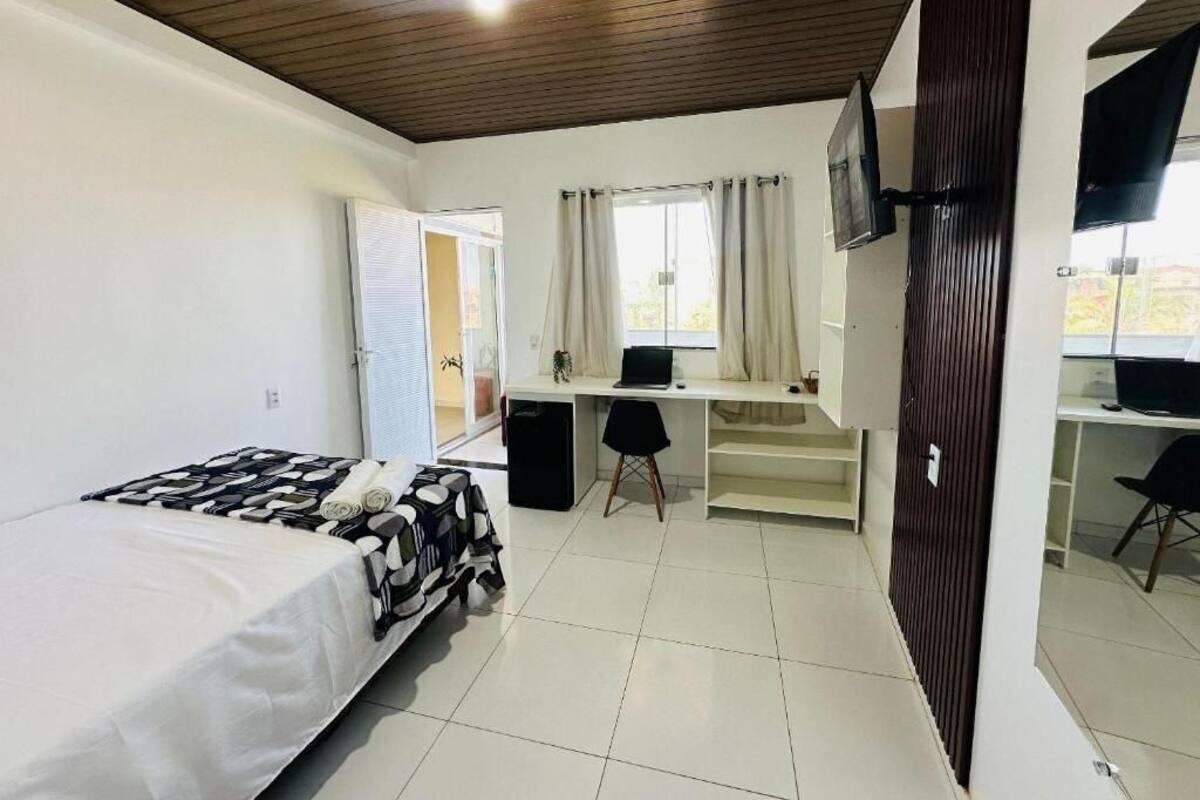 Une chambre à coucher avec un lit, un bureau, une chaise, un téléviseur et une fenêtre avec des rideaux.
