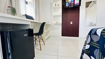 Quarto de hotel moderno com um frigorífico preto, uma escrivaninha com cadeira, uma televisão na parede e um sofá estampado.