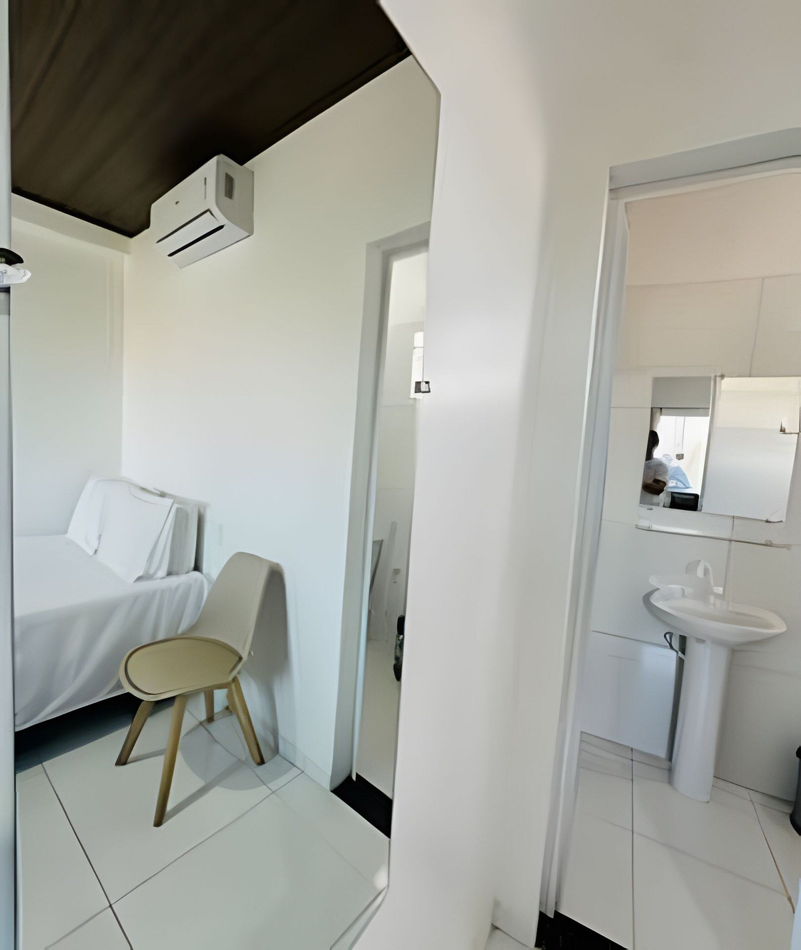 A hotel room with a bed, a chair, a sink, and a mirror.
