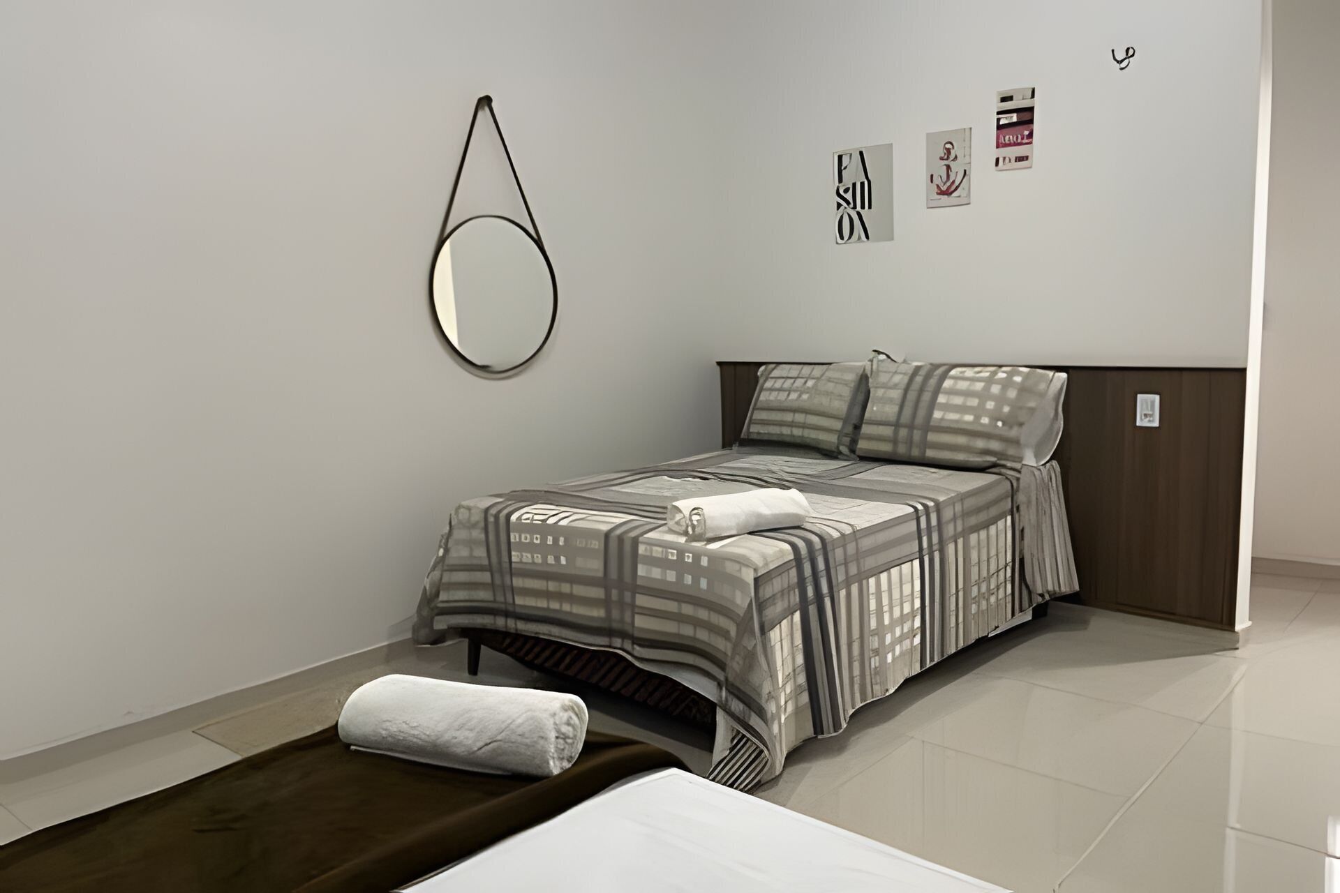 Une chambre bien rangée, avec un lit, une table de chevet, un miroir suspendu et un petit tapis.