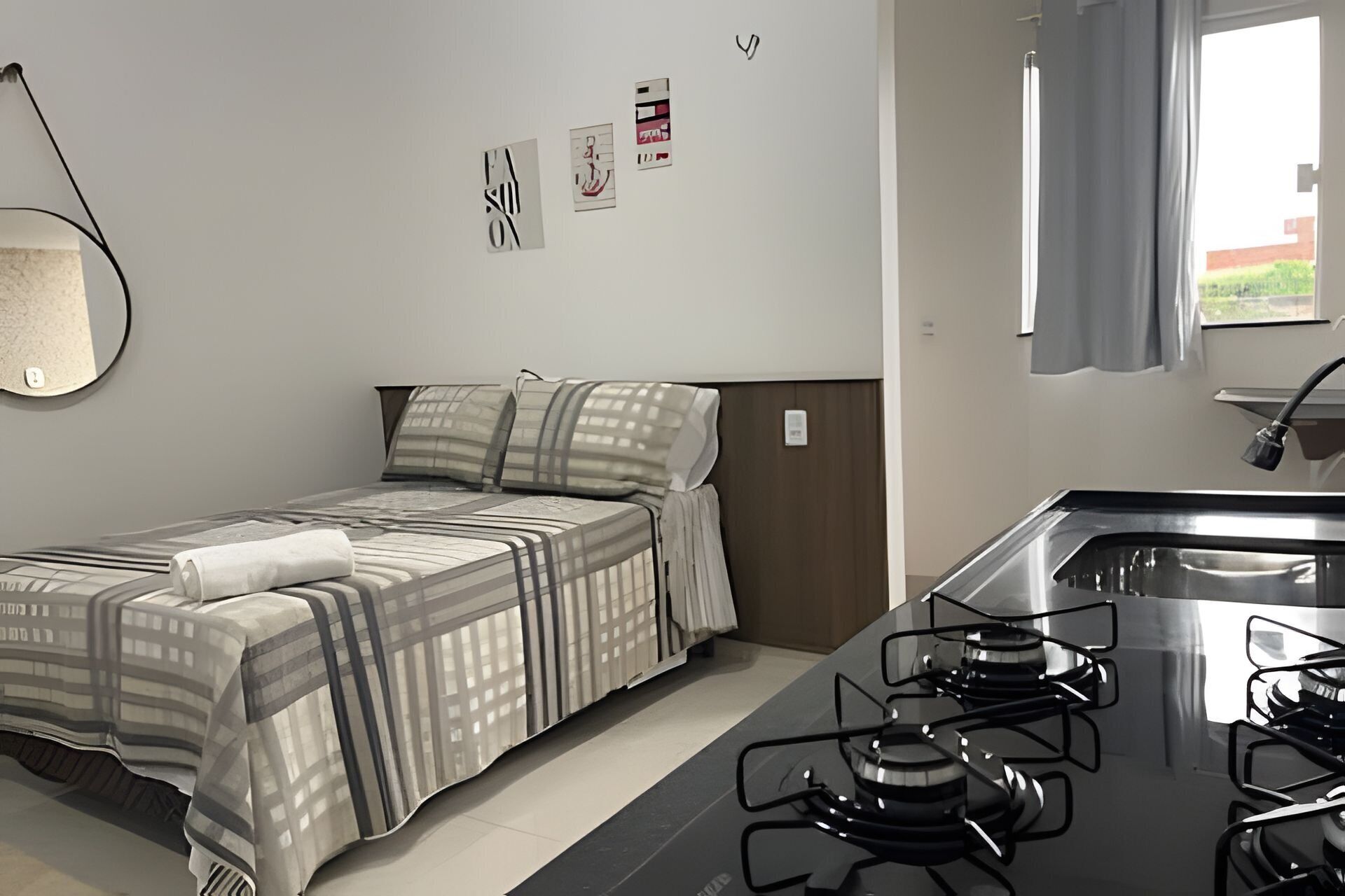 Una habitación de hotel compacta con cama, una kitchenette pequeña, un espejo y una ventana con cortinas.