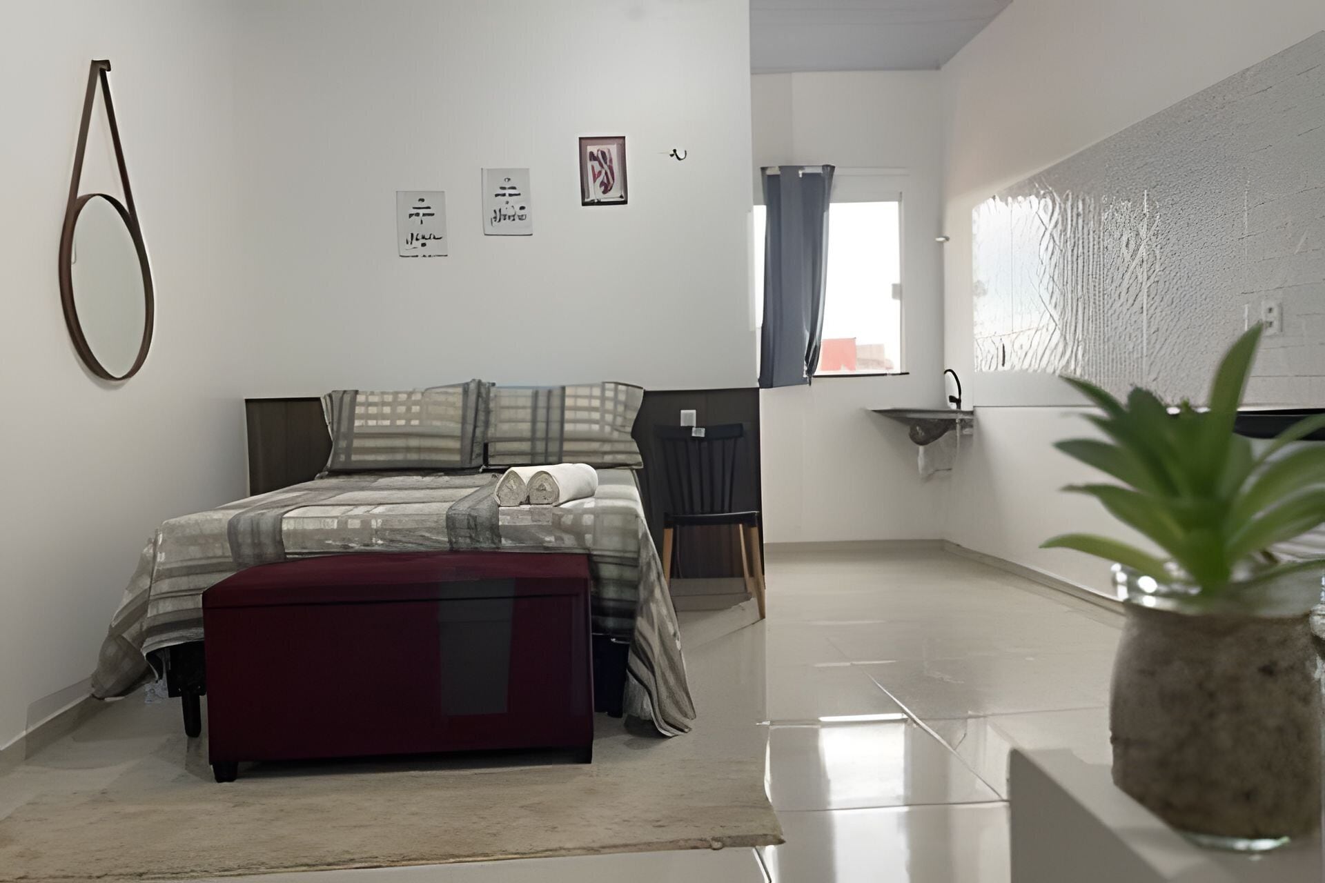 A modern bedroom with a bed, a small desk, a plant, and a bathroom visible through an open door.