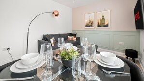 A dining area with a glass table set for four, surrounded by a modern living space with a sofa and a lamp. - Modern Luxury 4Bdrm Duplex | Business/Vacay | 15min to LDN centre | Free Parking (London)