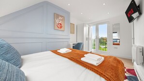 A modern hotel room with a large bed, a flat-screen TV mounted on the wall, and a balcony with a view. - Modern Luxury 4Bdrm Duplex | Business/Vacay | 15min to LDN centre | Free Parking (London)