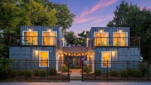 Ein modernes, zweistöckiges Containerhaus mit befestigtem Eingangsbereich, beleuchteten Fenstern und einer kleinen Außenlounge.
