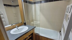 Un bagno moderno con un mobile bagno in legno, un lavandino bianco, box doccia in vetro e una vasca da bagno bianca.