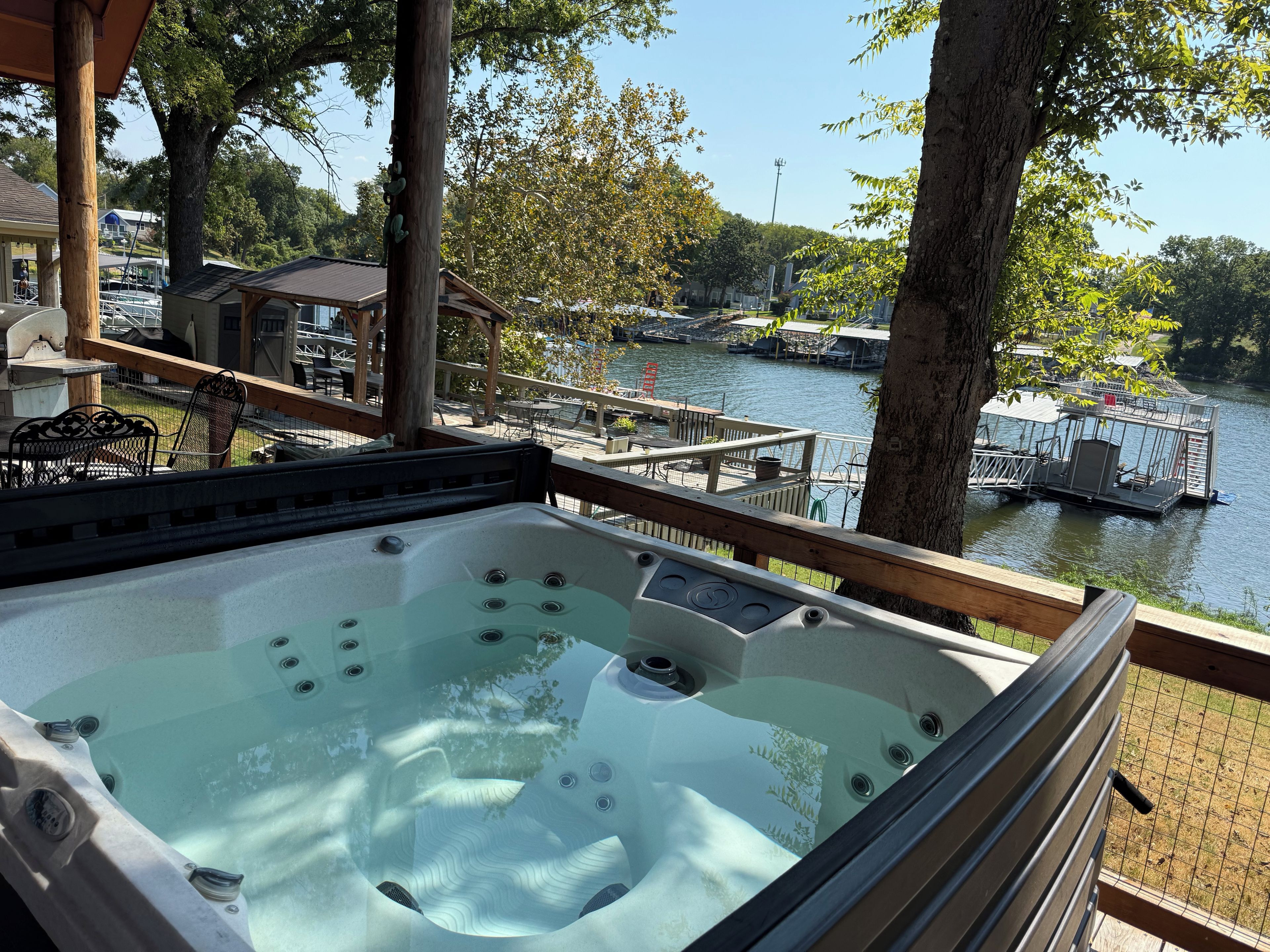 Un bain à remous sur une terrasse en bois donnant sur un lac, avec des quais et des bateaux.