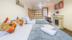 Une chambre d’hôtel avec deux lits, une cheminée, un bureau et un grand tableau au mur.