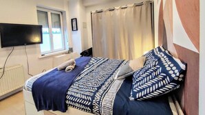 A bedroom with a bed, a flat-screen TV, a window with curtains, and a radiator.