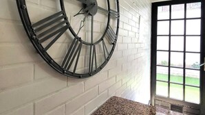 Un reloj grande de pared con números romanos en una habitación con paredes de ladrillo blanco y encimera de granito.